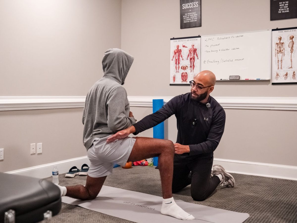 Eric Paige checking a client's knee and hip alignment in a half-kneeling position during a movement assessment