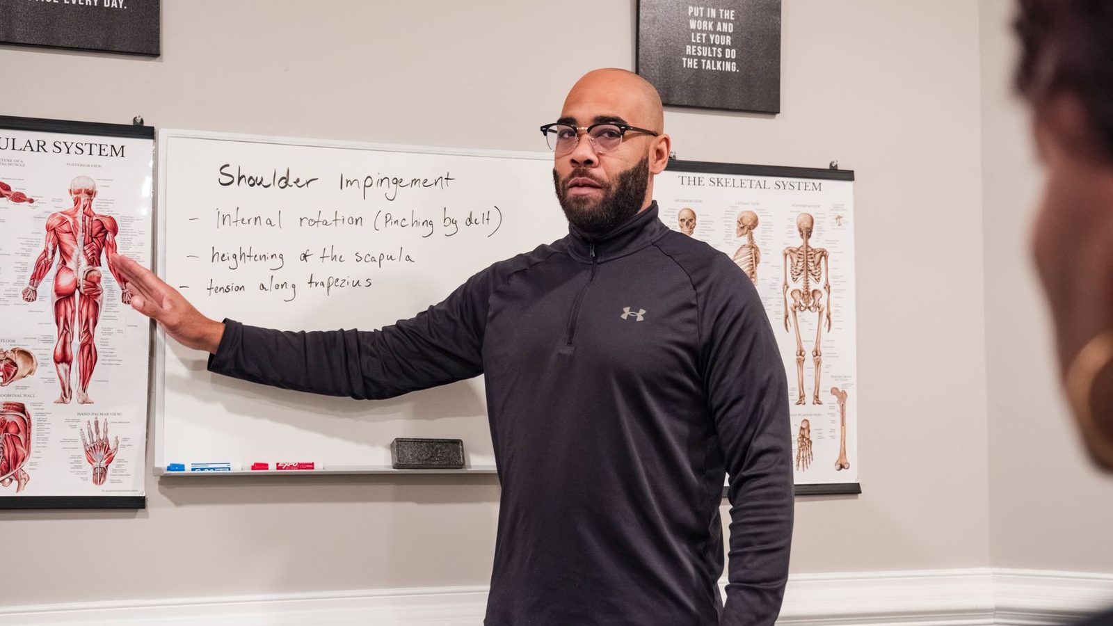 Eric Paige explaining shoulder mechanics at an anatomy chart during a client session in his Raleigh studio