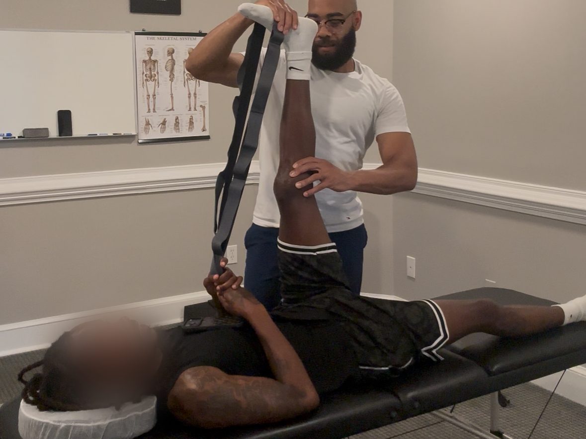 Eric Paige guiding a strap-assisted hamstring stretch with a client on a treatment table