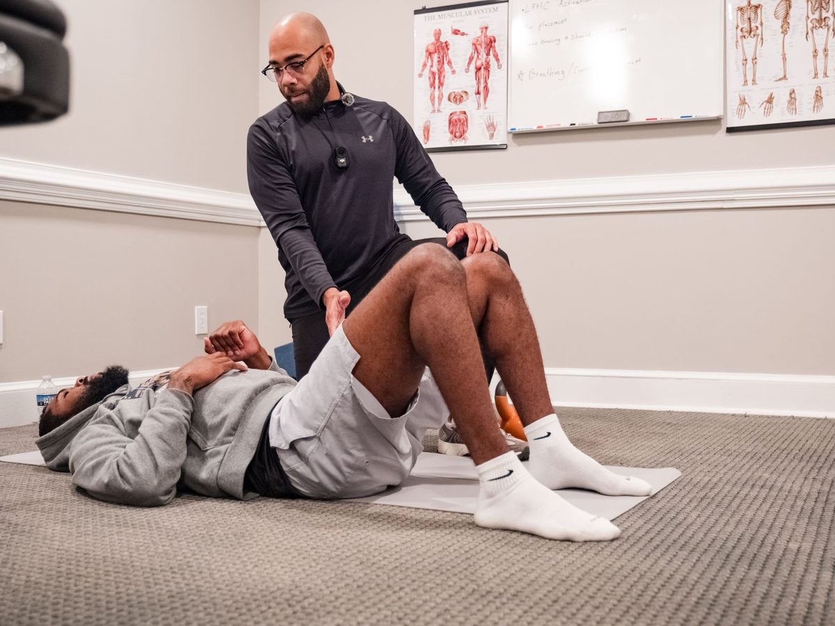 Eric Paige guiding a client through an assisted hip and hamstring stretch on a mat