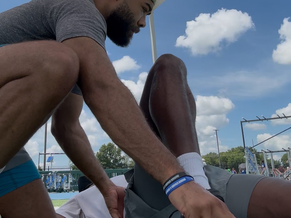 Eric Paige working on an athlete's ankle trackside under a treatment tent at a meet
