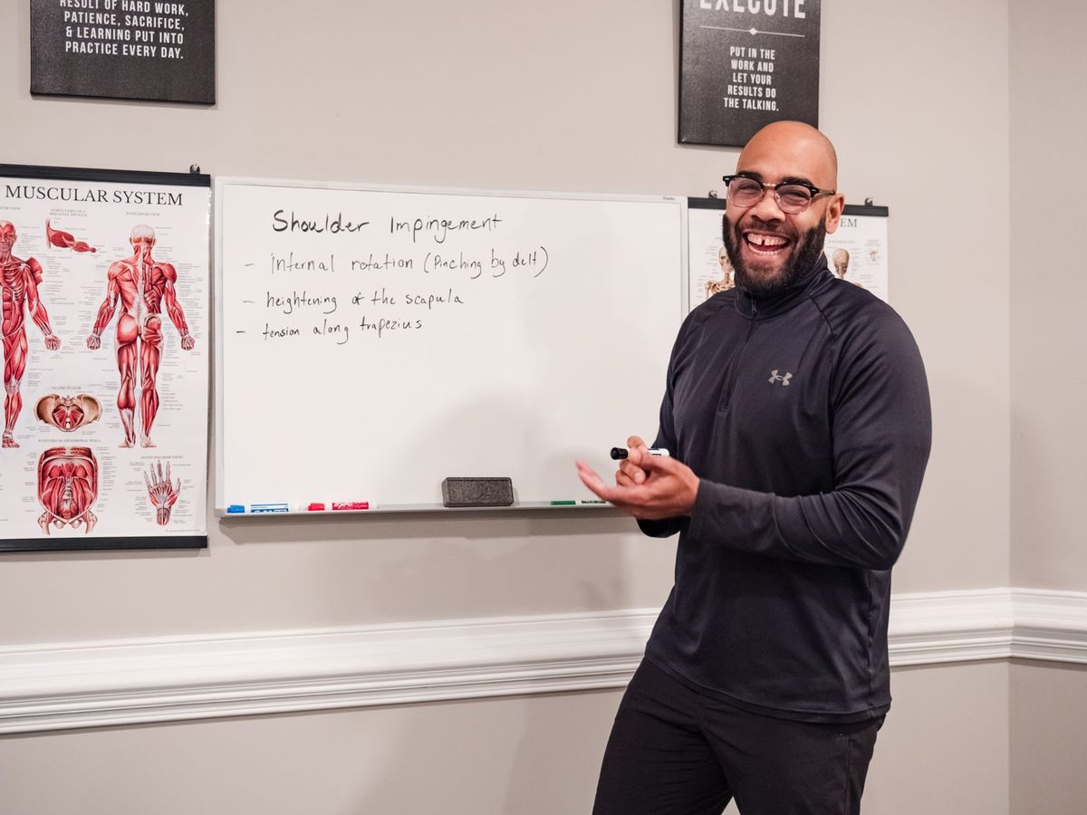 Eric Paige teaching at the whiteboard beside a muscular system chart